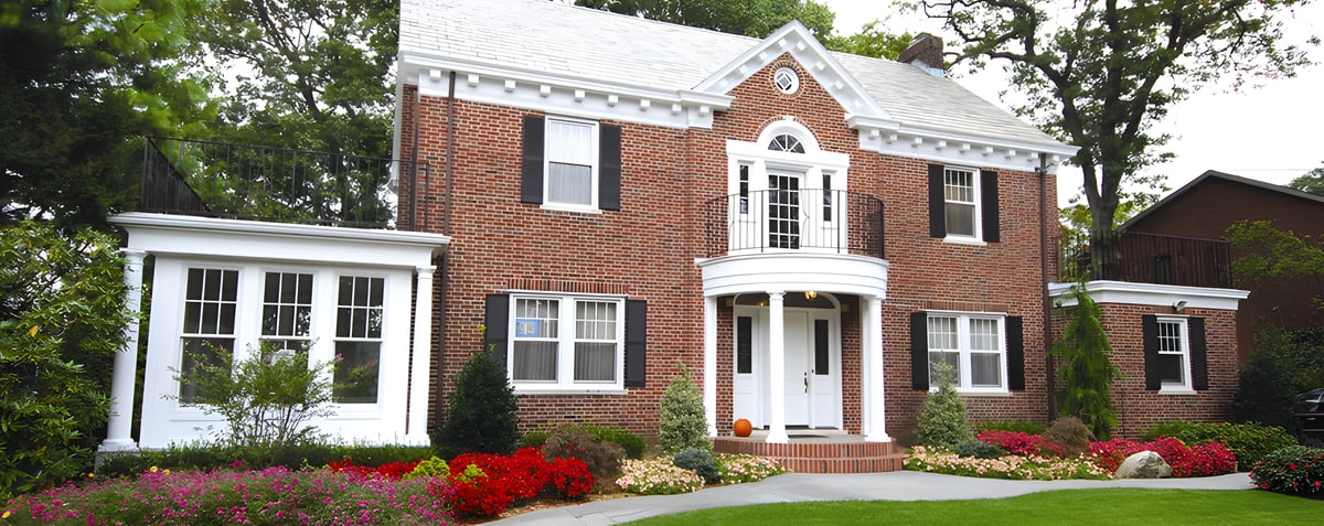 Red brick colonial house with white portico and flower beds