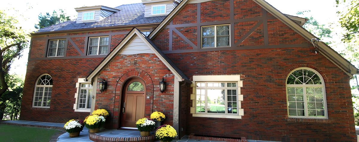 Red brick Tudor-style house with arched wooden door and mums